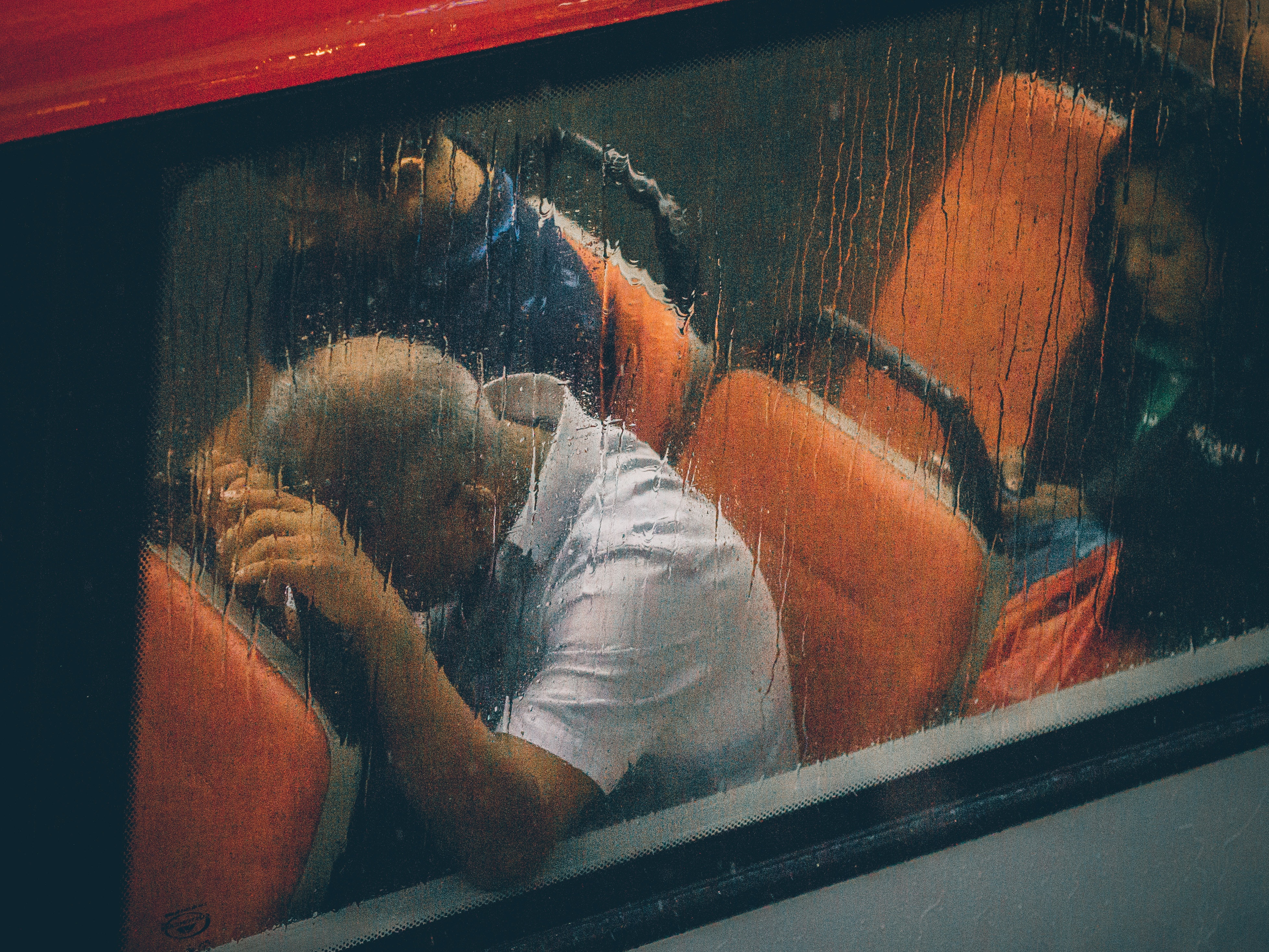 Exhausted man slumps over the seat in front of him in a bus, while the rain runs down the window.