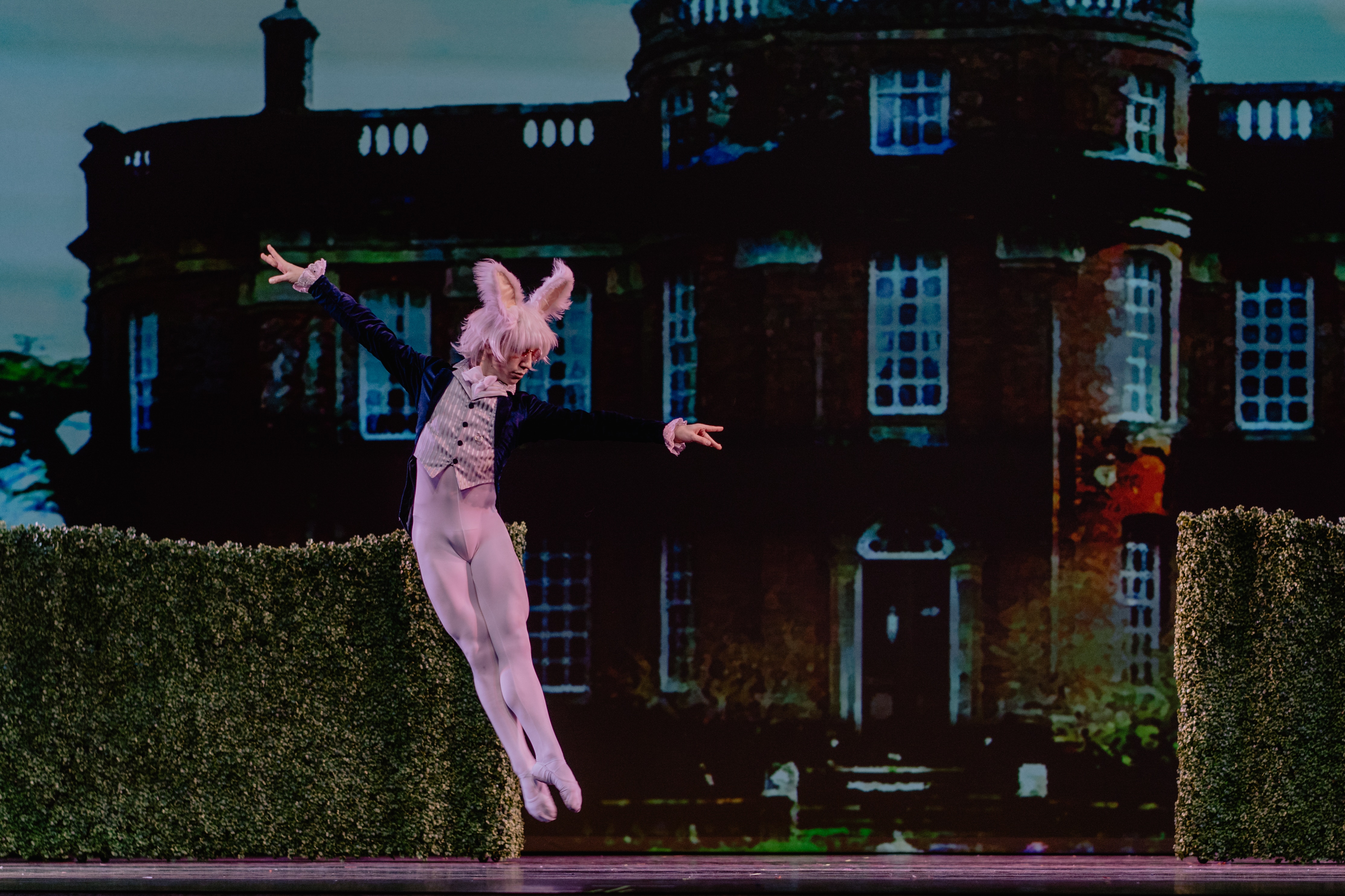 Male ballet dancer in a pink rabbit costume and a coat, leaping in the street.